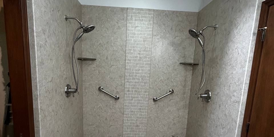 Walk-in shower finished in grout-free solid-surface panels with twin shower heads and grab bars
