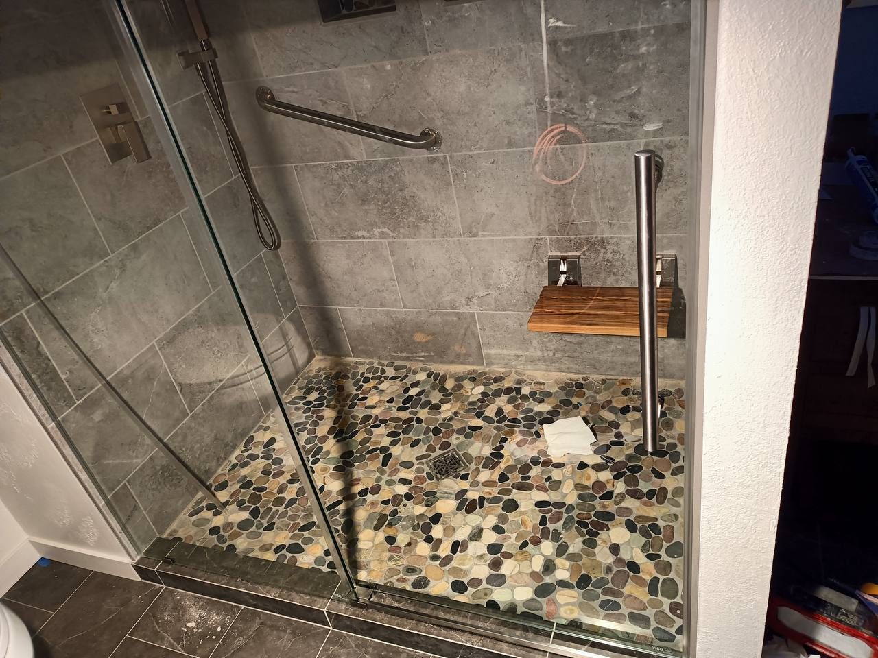 Walk-in tile shower with river-pebble floor, grab bar and glass panel