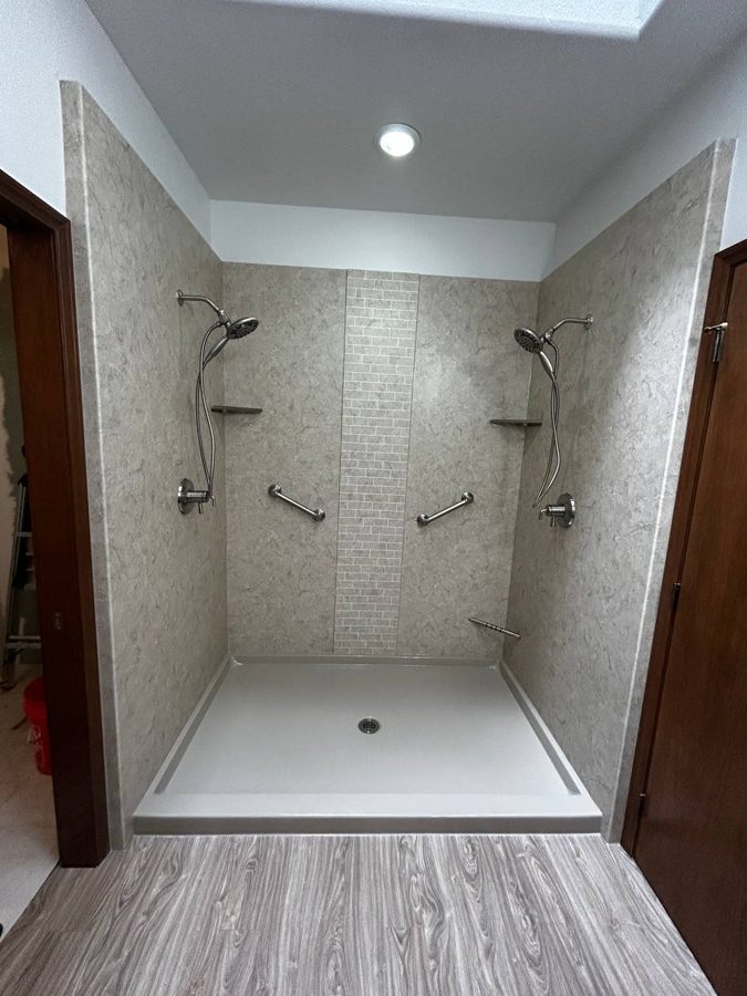 Finished walk-in shower in grout-free solid-surface panels with twin shower heads, grab bars and a tile accent stripe