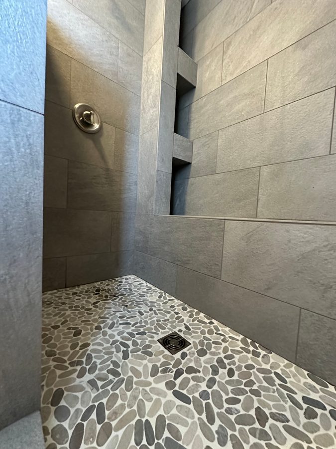 Walk-in tile shower with niche shelves and pebble floor