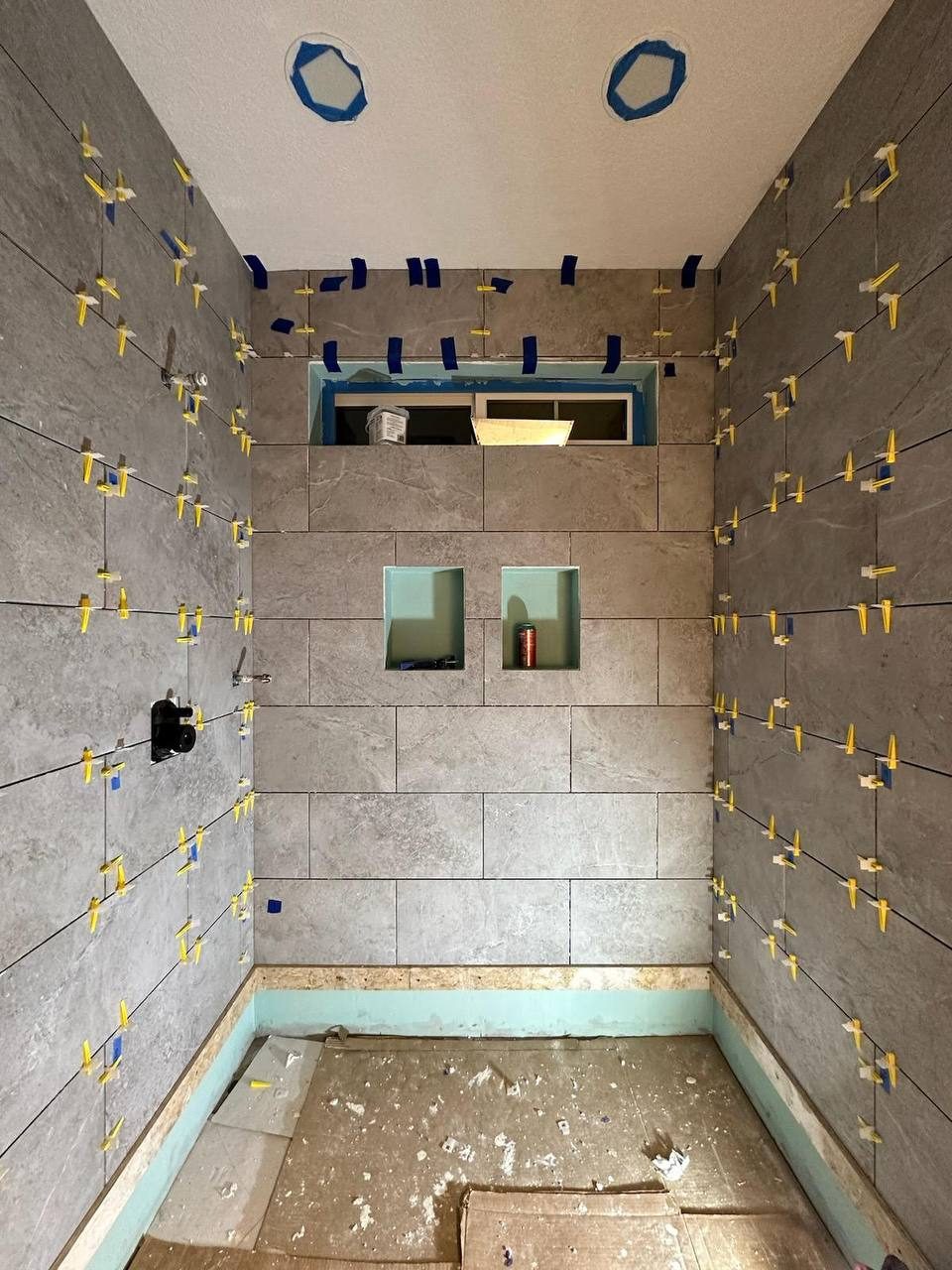Large-format shower tile being set with leveling spacers β floor-to-ceiling custom tile work in progress