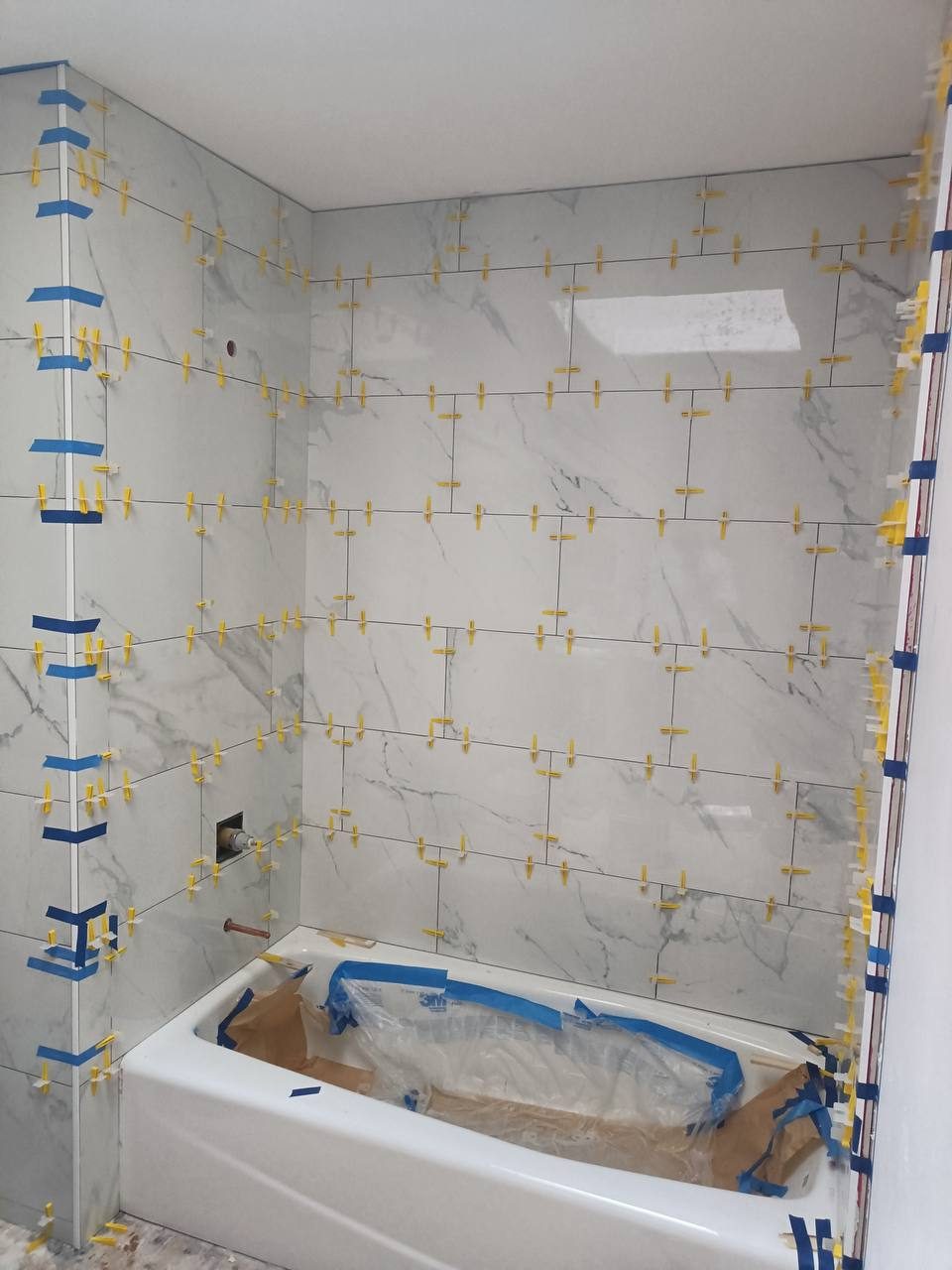 New tub with marble-look tile surround mid-install, leveling clips still in place